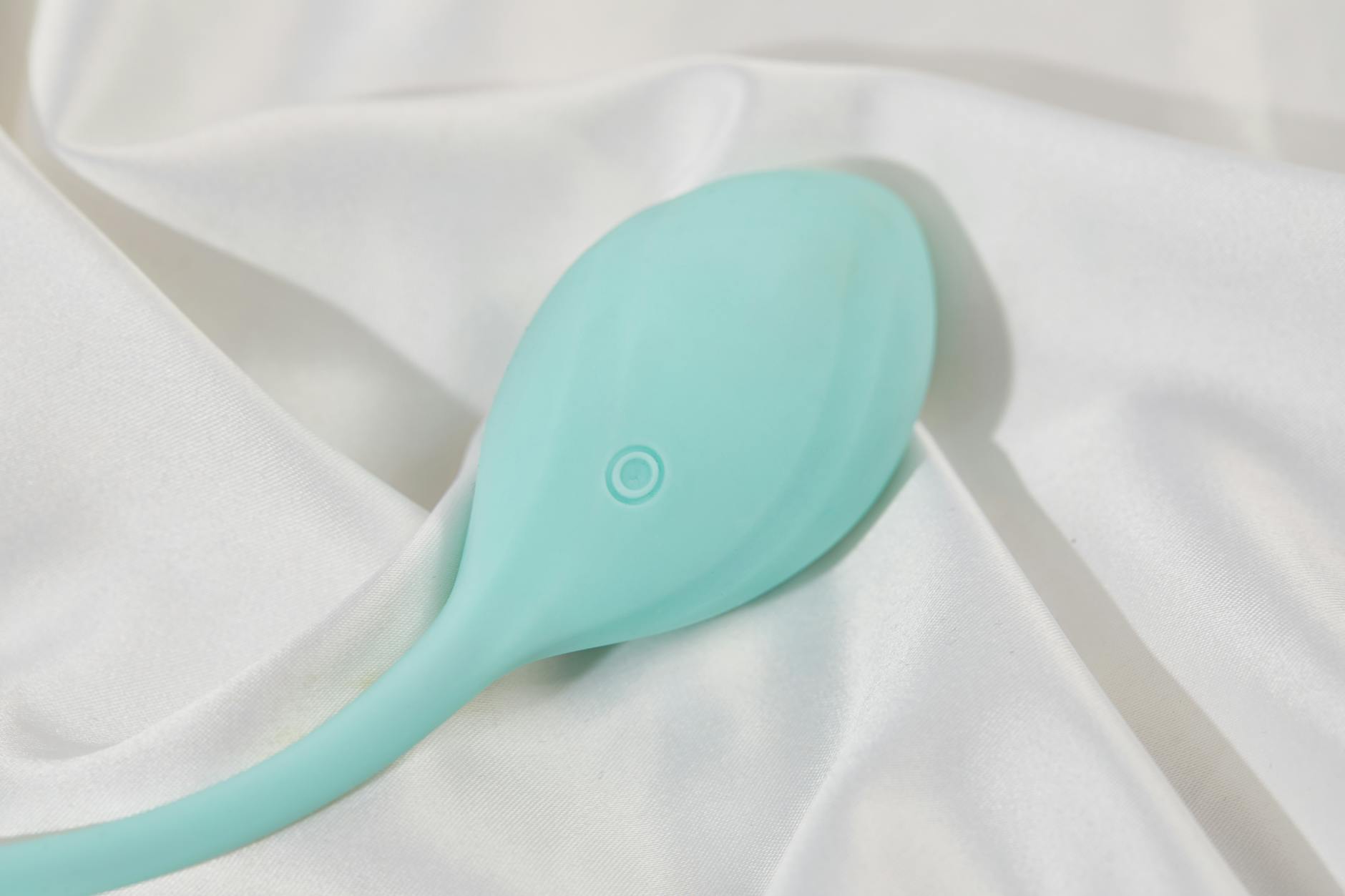 A sleek teal lemon clitoral vibrator on soft white silk, representing modern intimate wellness
