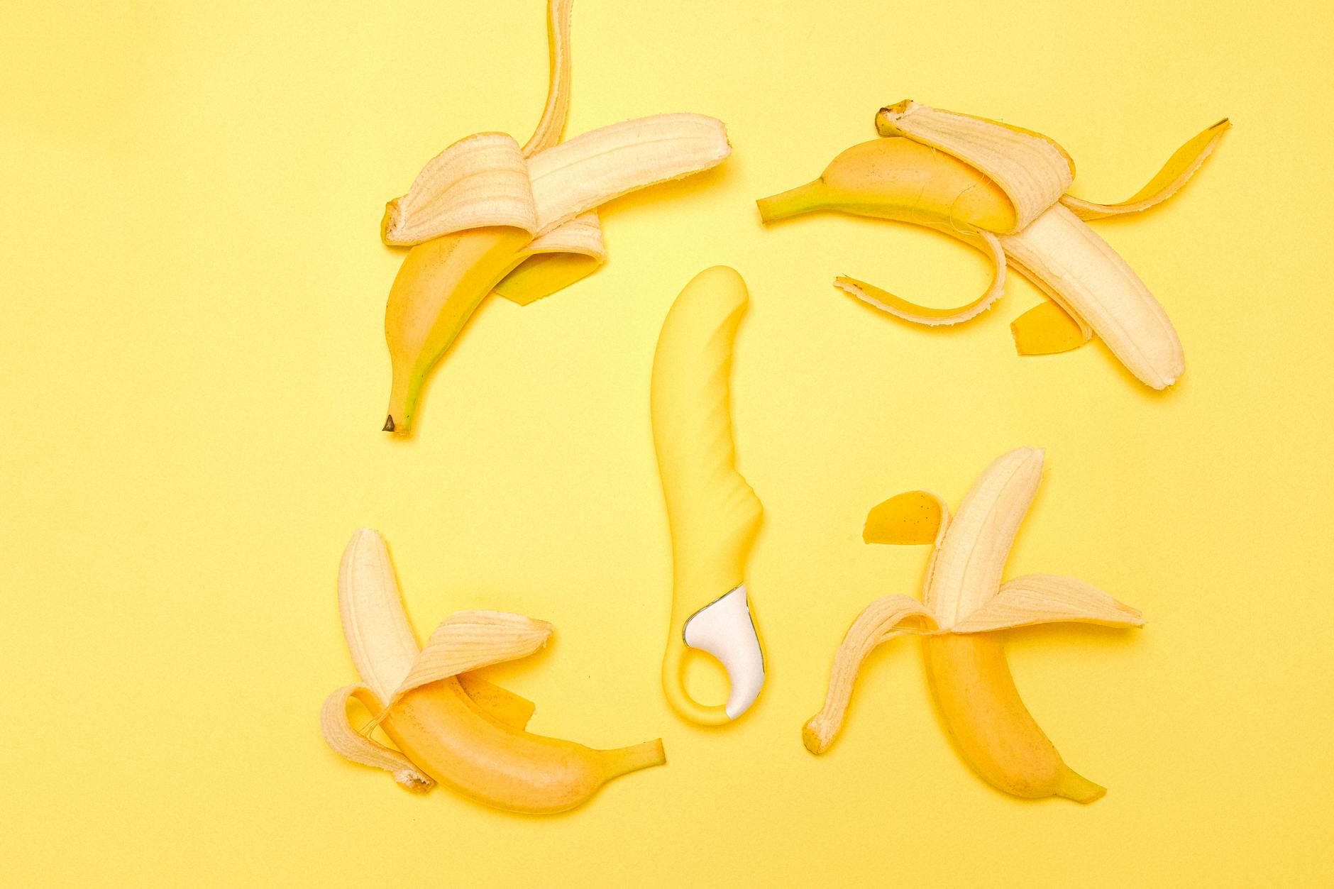 Bright yellow lemon-shaped vibrator with fresh lemons on a yellow background