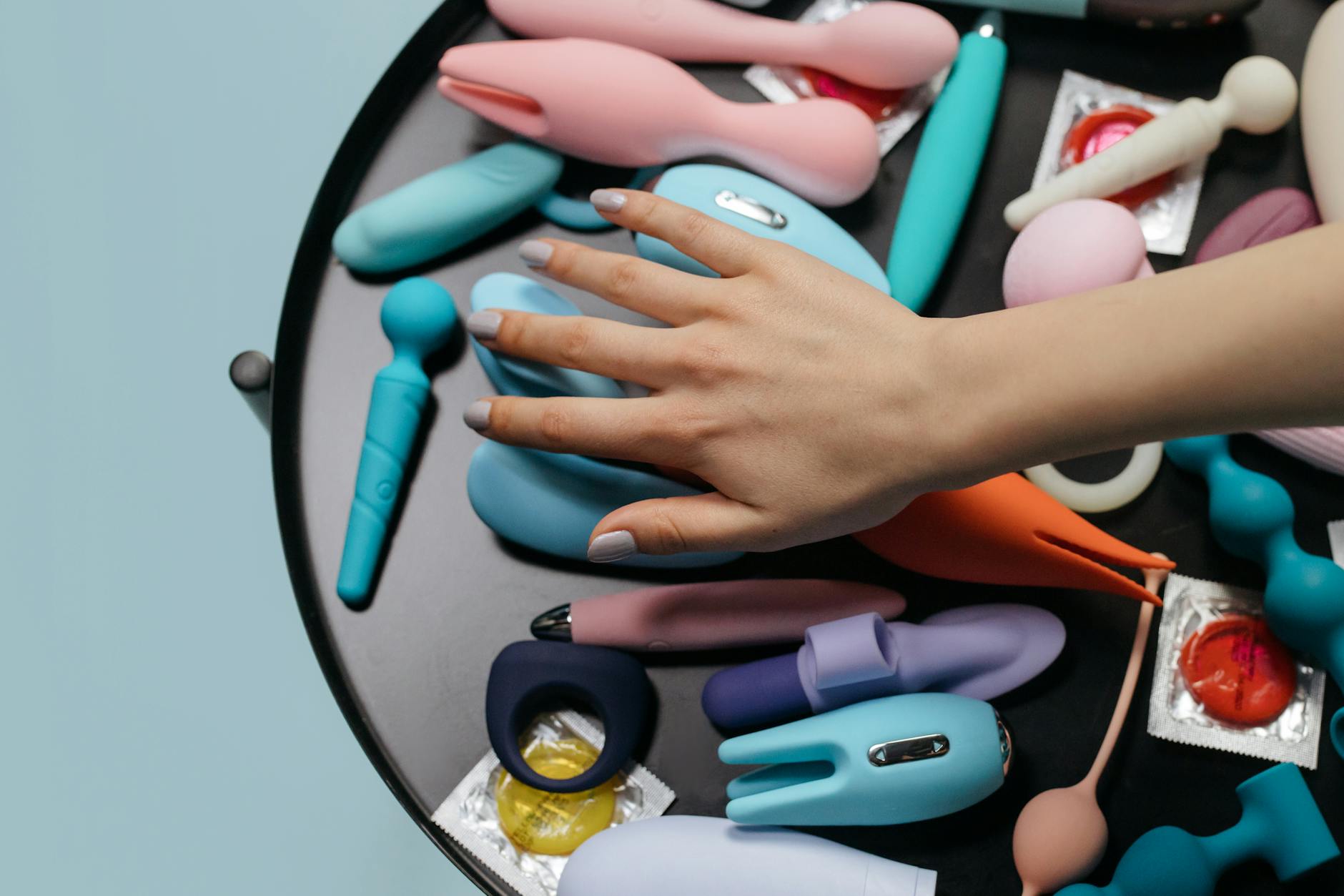A hand reaching over a variety of colorful sex toys including lemon vibrators arranged on a table.