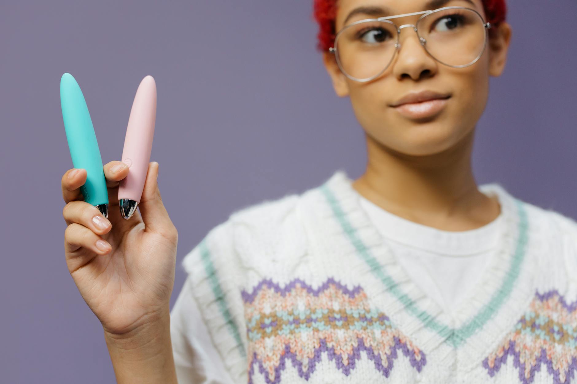 A young woman holding colorful vibrators against a purple background, representing pleasure and choice after menopause.