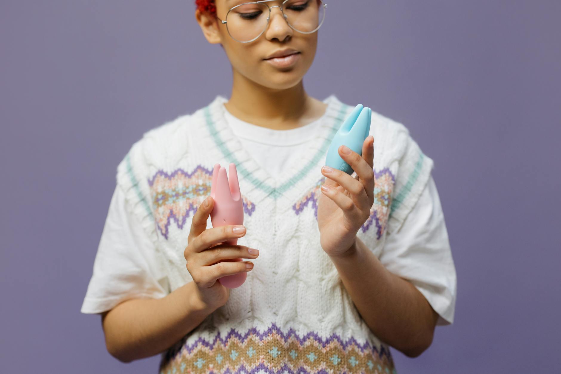 Woman holding blue and pink silicone vibrators thoughtfully against a calm background