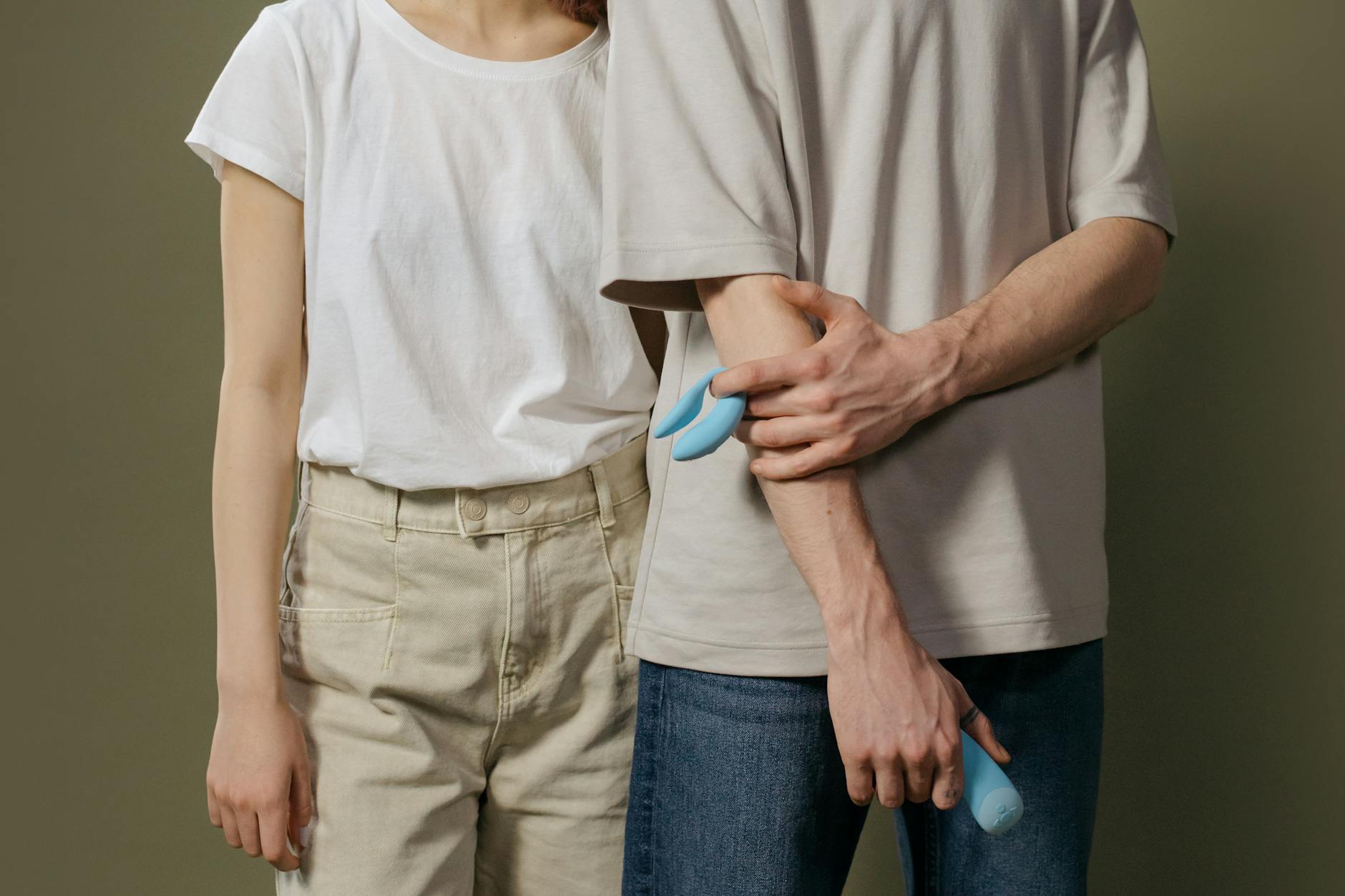 A young couple standing together indoors, holding a blue vibrator, symbolizing modern intimacy and shared pleasure exploration.