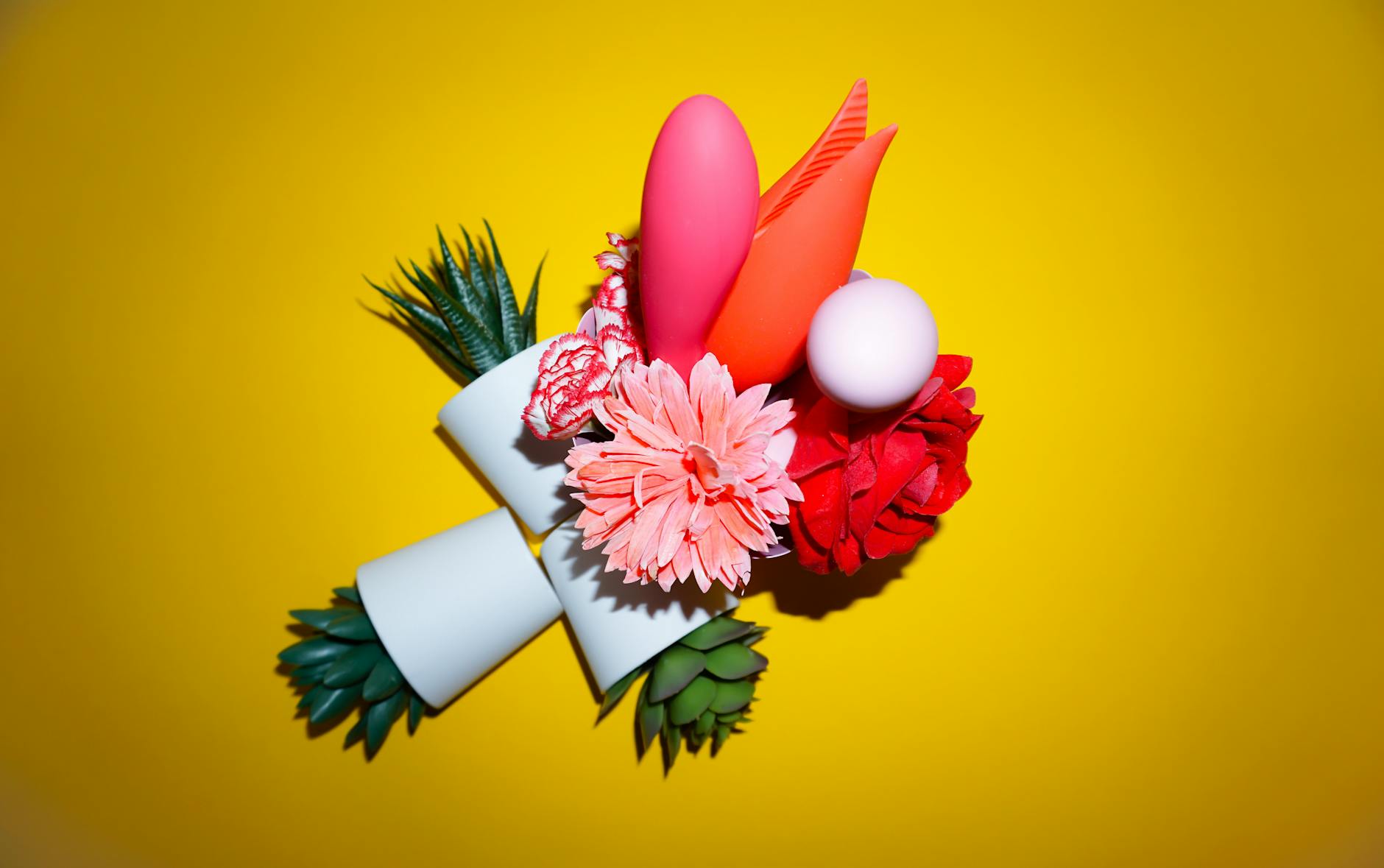 A blue clitoral vibrator surrounded by flowers and citrus on a yellow background